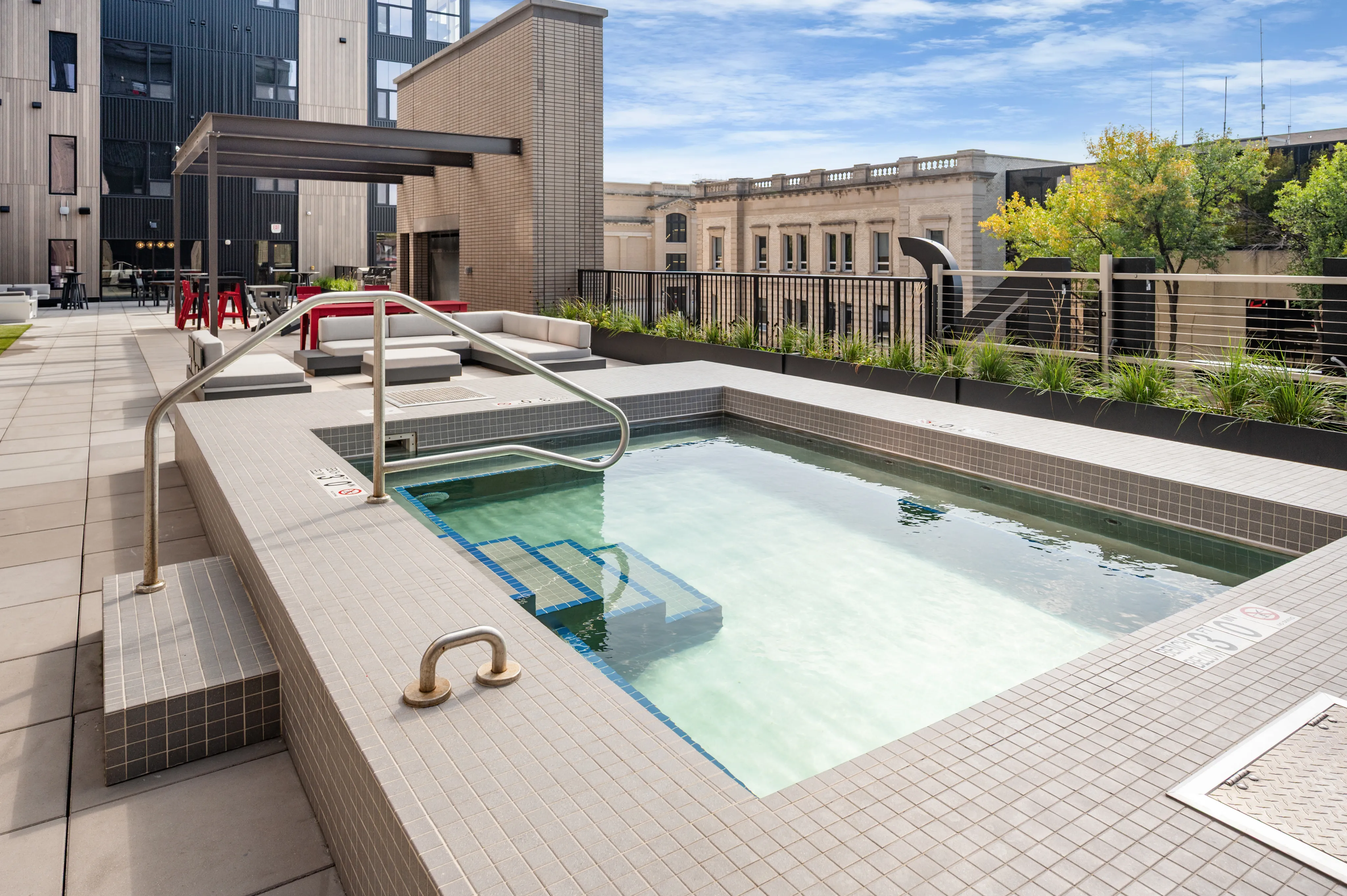 Modern rooftop terrace featuring a sleek pool with elegant tiling, stylish lounge seating, and vibrant city views.