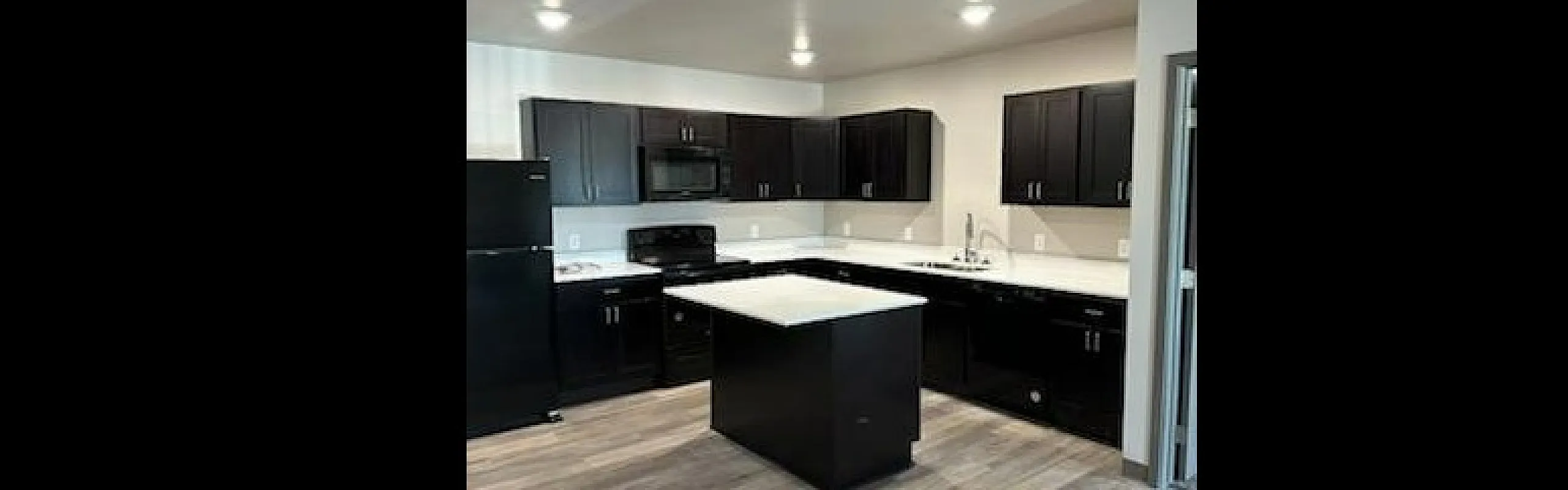 Sleek kitchen featuring dark cabinetry, an island with a marble countertop, and contemporary lighting.