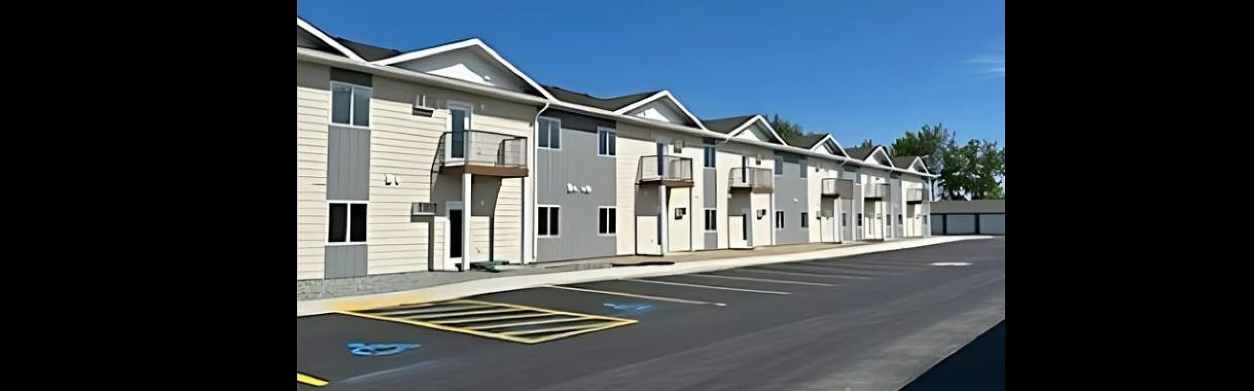 Contemporary two-story apartment building with balconies and ample parking under a bright blue sky.