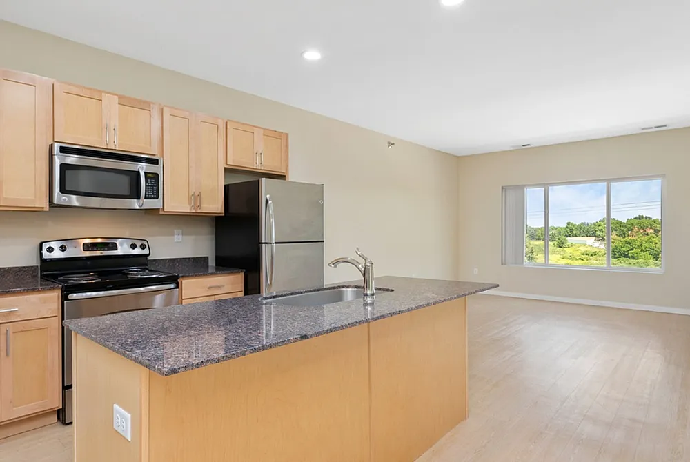 Inviting open-concept kitchen with modern appliances, granite countertops, and elegant wood cabinetry leading to a bright living space with scenic window views.