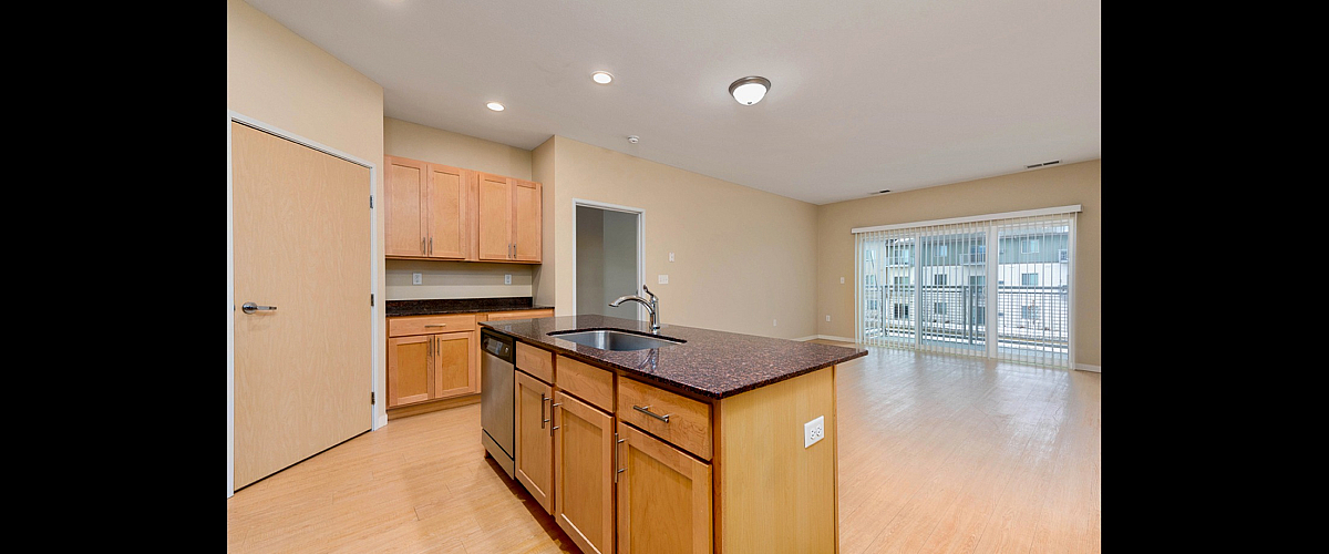 Bright open-concept kitchen and living area with sleek granite countertops, elegant cabinetry, and large sliding glass doors to a private balcony.