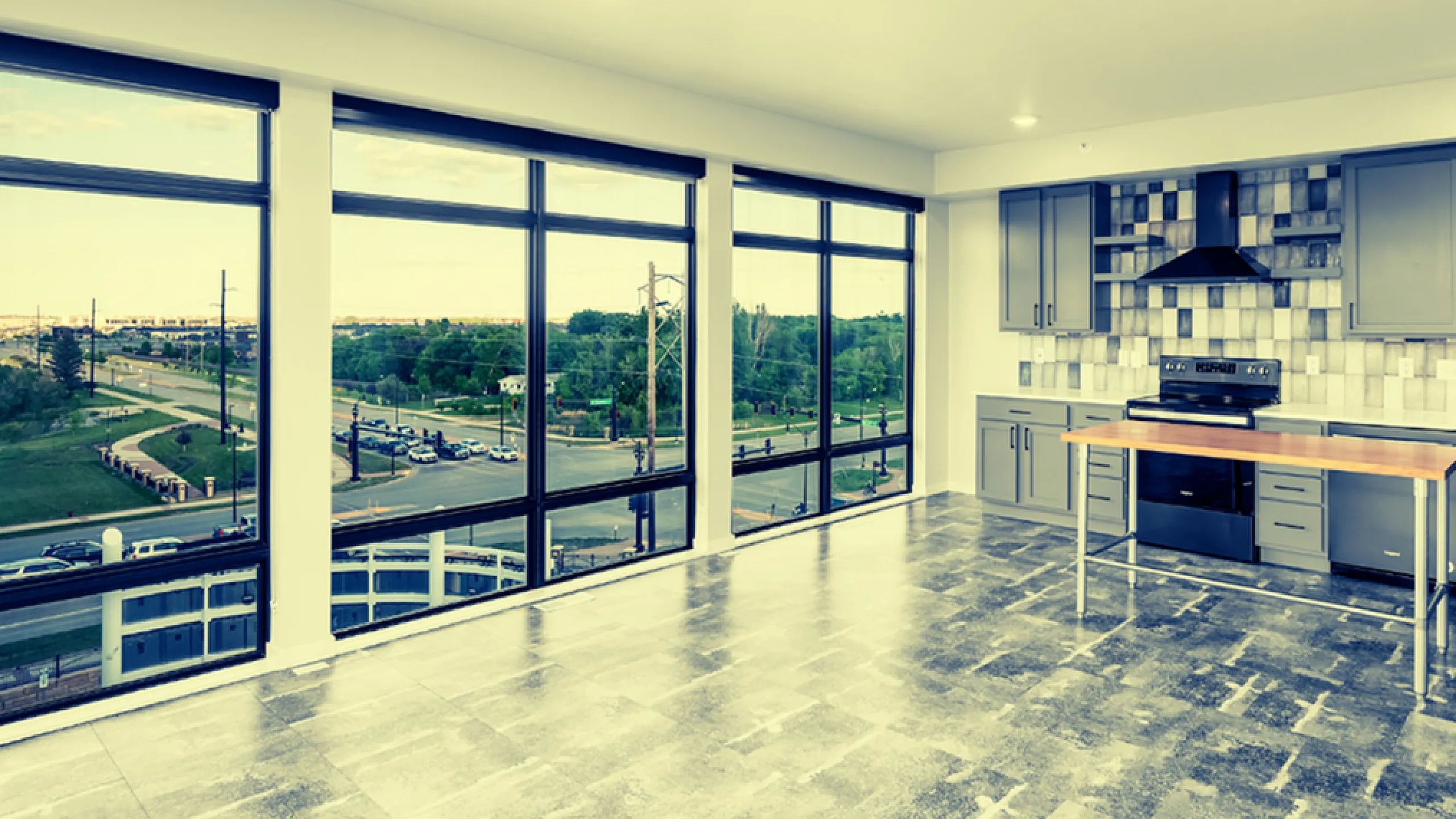Modern apartment with expansive floor-to-ceiling windows offering stunning city views, sleek grey cabinetry, and a chic tiled backsplash in the kitchen.