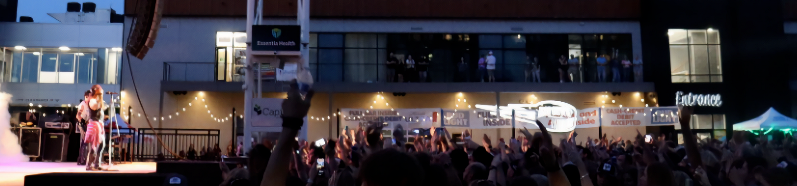 Vibrant evening concert event with a lively crowd, stage lights, and modern apartment building backdrop.