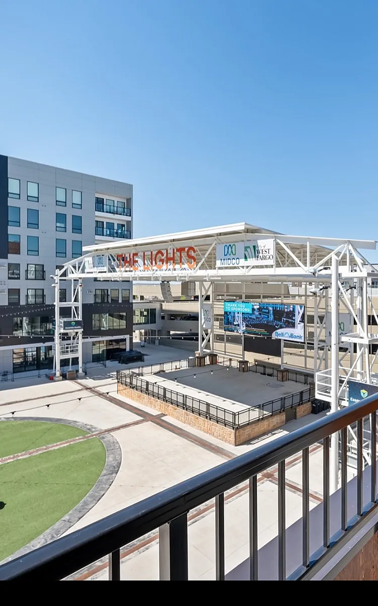 Chic urban balcony view overlooking vibrant venue space with modern architecture and bright green outdoor area.