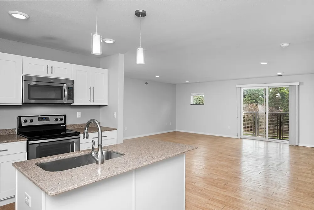 Bright and modern open-concept living space featuring a sleek kitchen with granite countertops, stainless steel appliances, and expansive hardwood flooring leading to a balcony with scenic views.