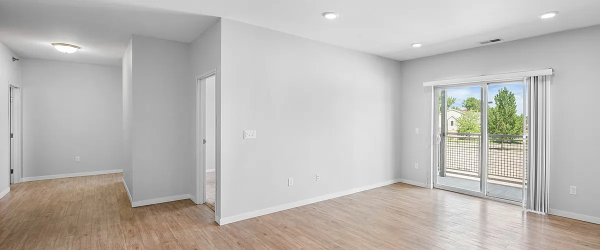 Bright and open living space with wood flooring, natural light, and sliding glass doors leading to a balcony.