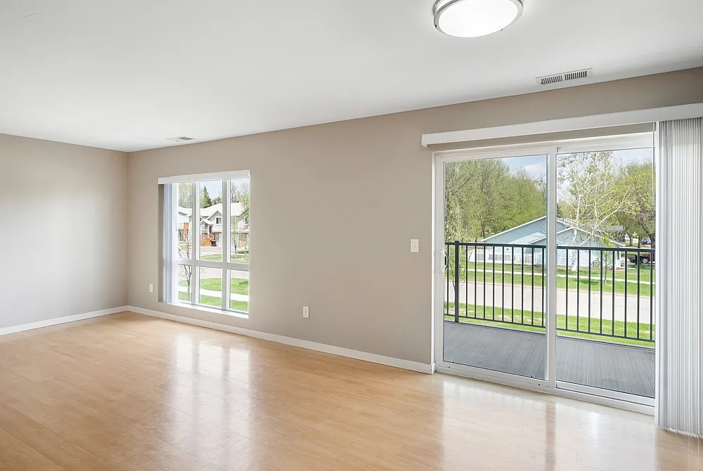 Bright and spacious living room with modern wood flooring, large windows, and a balcony with a scenic view of a green neighborhood.