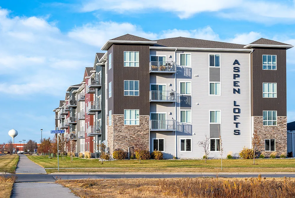 Modern Aspen Lofts apartment building exterior with spacious balconies, surrounded by scenic landscapes and blue skies.