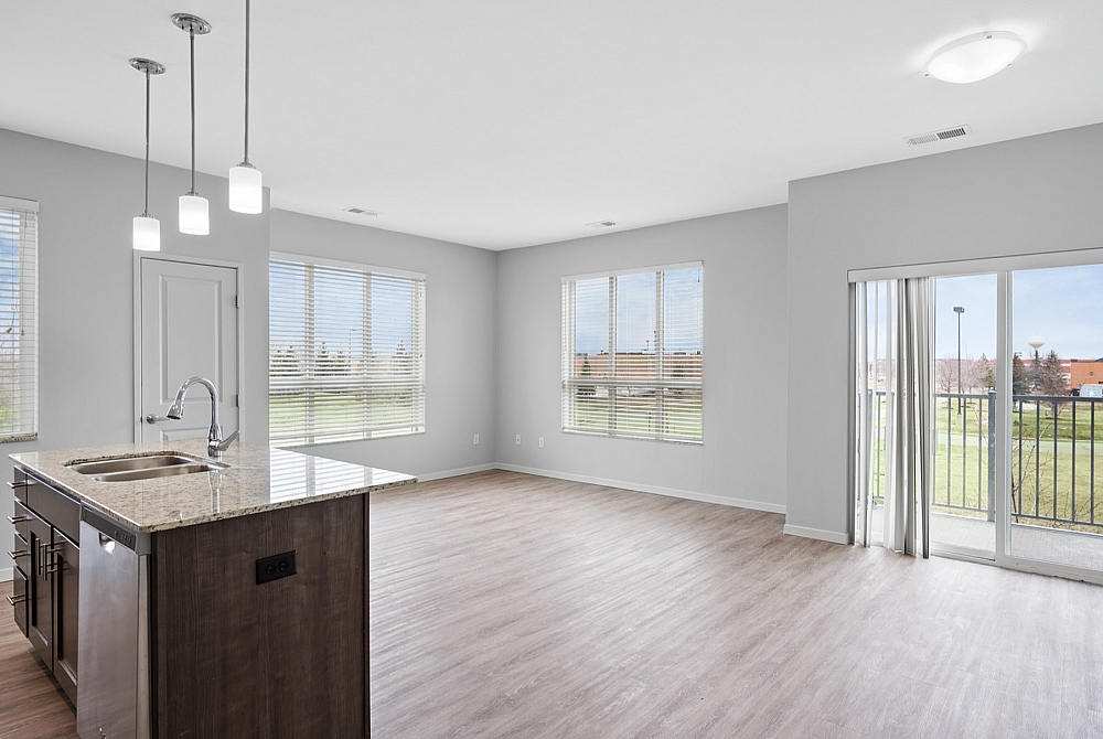 Bright and modern open-plan living space featuring a sleek kitchen island with granite countertops, large windows, and a private balcony view.