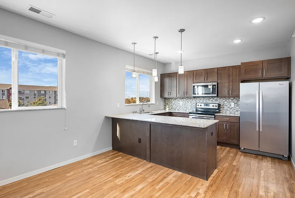 Contemporary kitchen with elegant granite countertops, stainless steel appliances, and warm wood cabinetry, complemented by abundant natural light from large windows.
