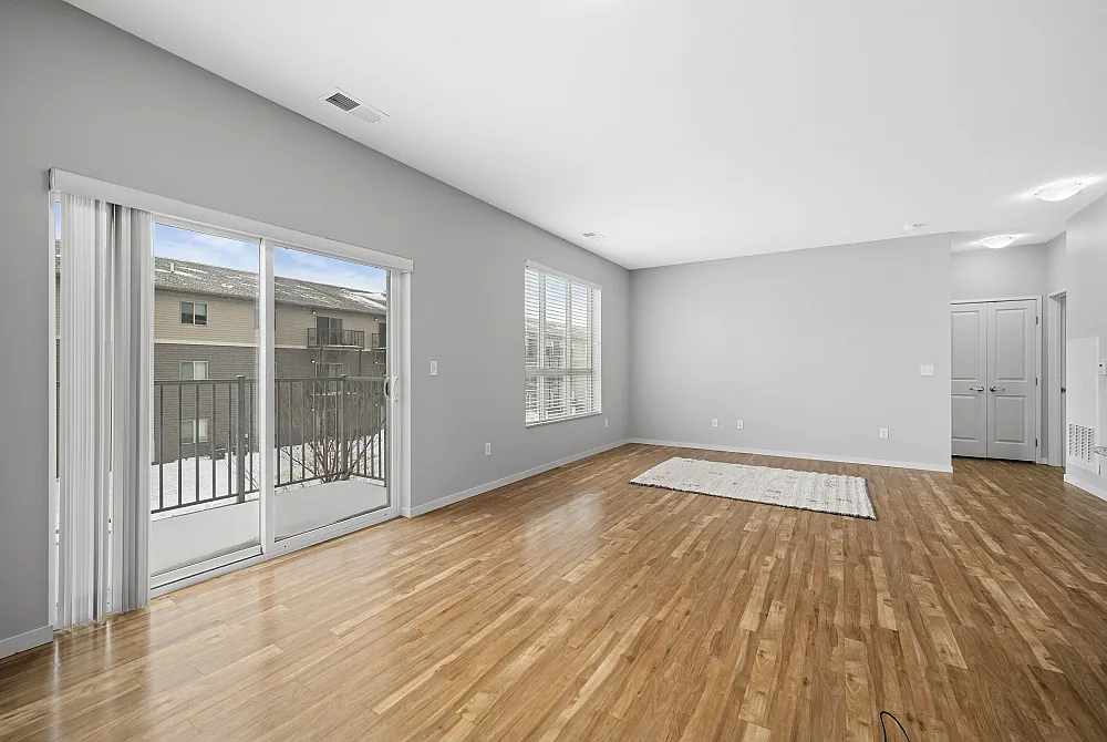 Bright and spacious living area with elegant hardwood flooring, large sliding glass doors opening to a balcony, and abundant natural light creating a warm and inviting atmosphere.