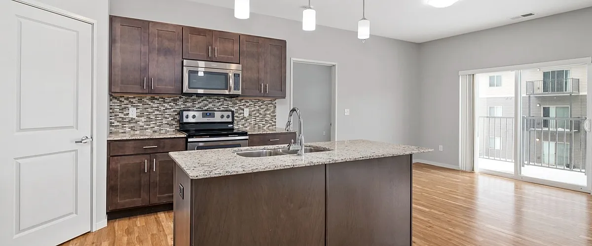 Modern kitchen with sleek granite countertops, stainless steel appliances, and elegant pendant lighting opening to a bright living area with natural wood flooring.