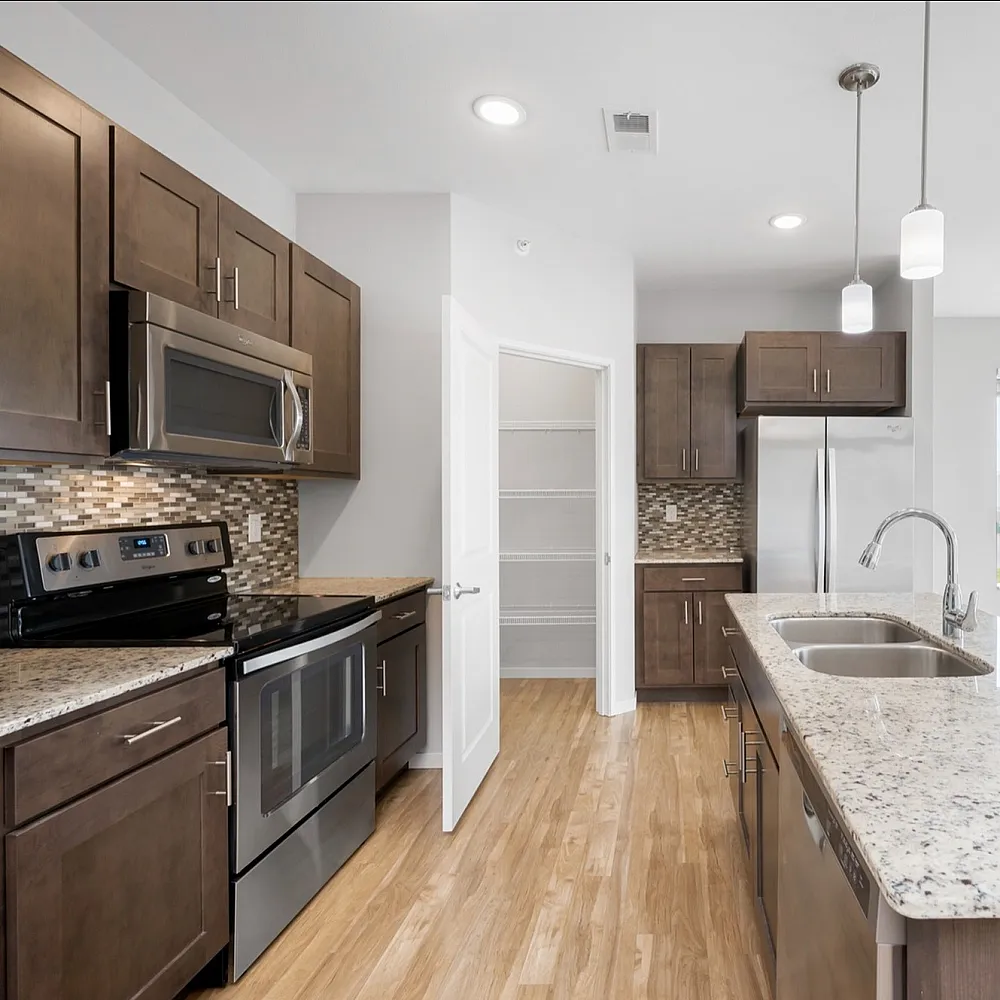 Modern kitchen with sleek wooden cabinets, stainless steel appliances, and a spacious island with granite countertops. Bright and airy space with elegant pendant lighting and views of the surrounding greenery through large windows.