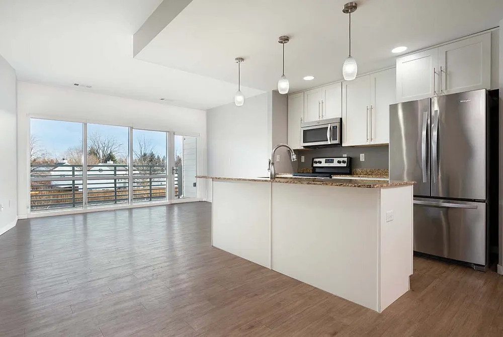 Bright open-concept kitchen and living area with sleek hardwood floors, modern stainless steel appliances, and elegant pendant lighting.