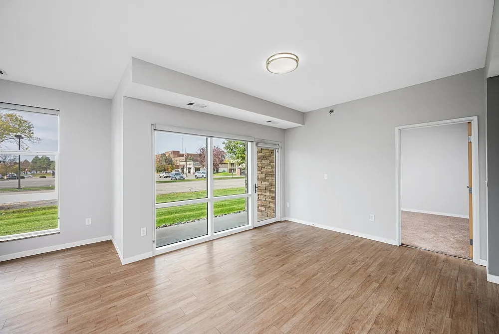 Bright and spacious living area with floor-to-ceiling windows, wood-style flooring, and inviting views of greenery.