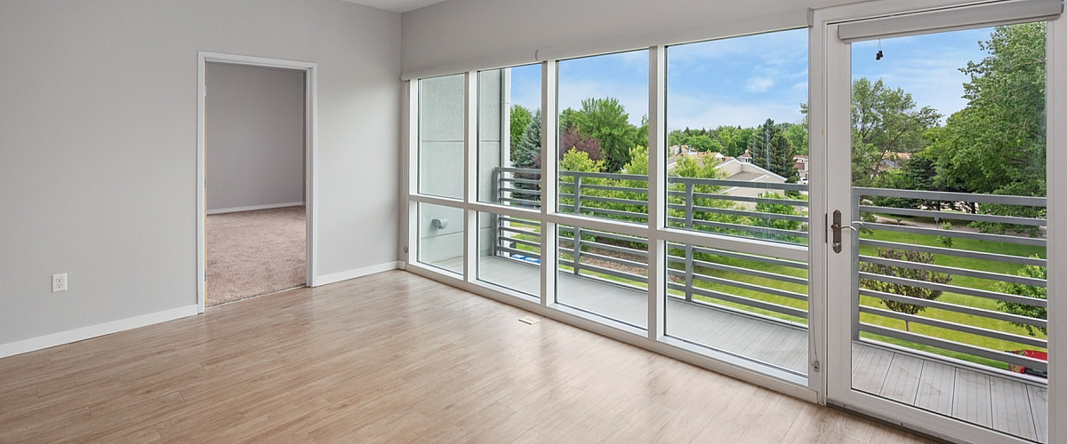 Bright living room with modern hardwood floors and large windows opening to a scenic balcony view.