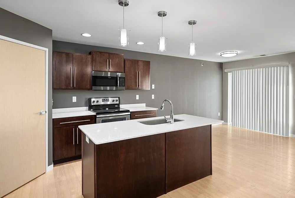 Modern open kitchen with a sleek island, stainless steel appliances, and elegant dark wood cabinets, illuminated by stylish pendant lights.