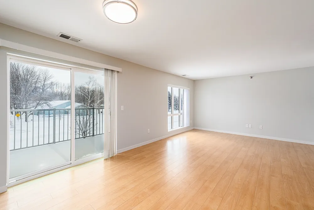 Bright, spacious living area with warm wooden floors and sliding doors opening to a scenic snowy balcony view.