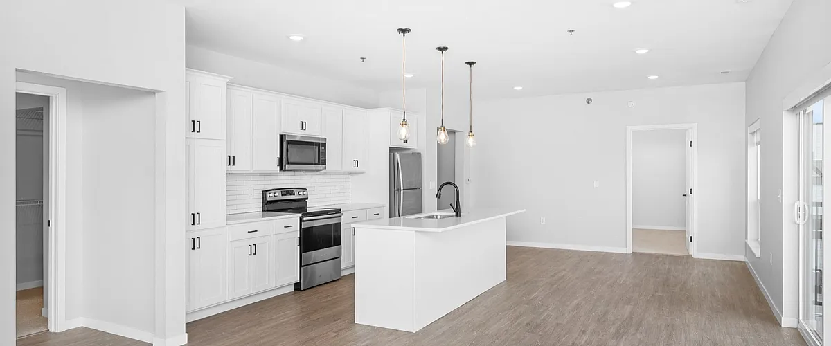 Modern open-plan kitchen with sleek white cabinetry, stainless steel appliances, and elegant pendant lighting in a spacious living area with hardwood floors.