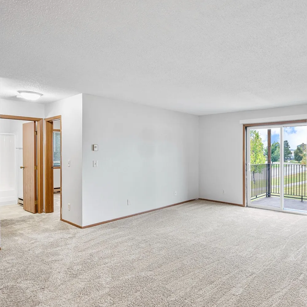 Bright living area with plush carpeting, large sliding glass doors leading to a balcony with a scenic view, and easy access to adjacent rooms.