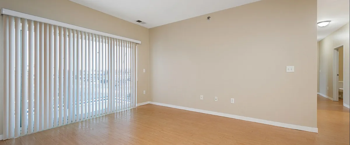 Bright and spacious living area with sleek hardwood floors and elegant sliding door with vertical blinds, perfect for modern living.