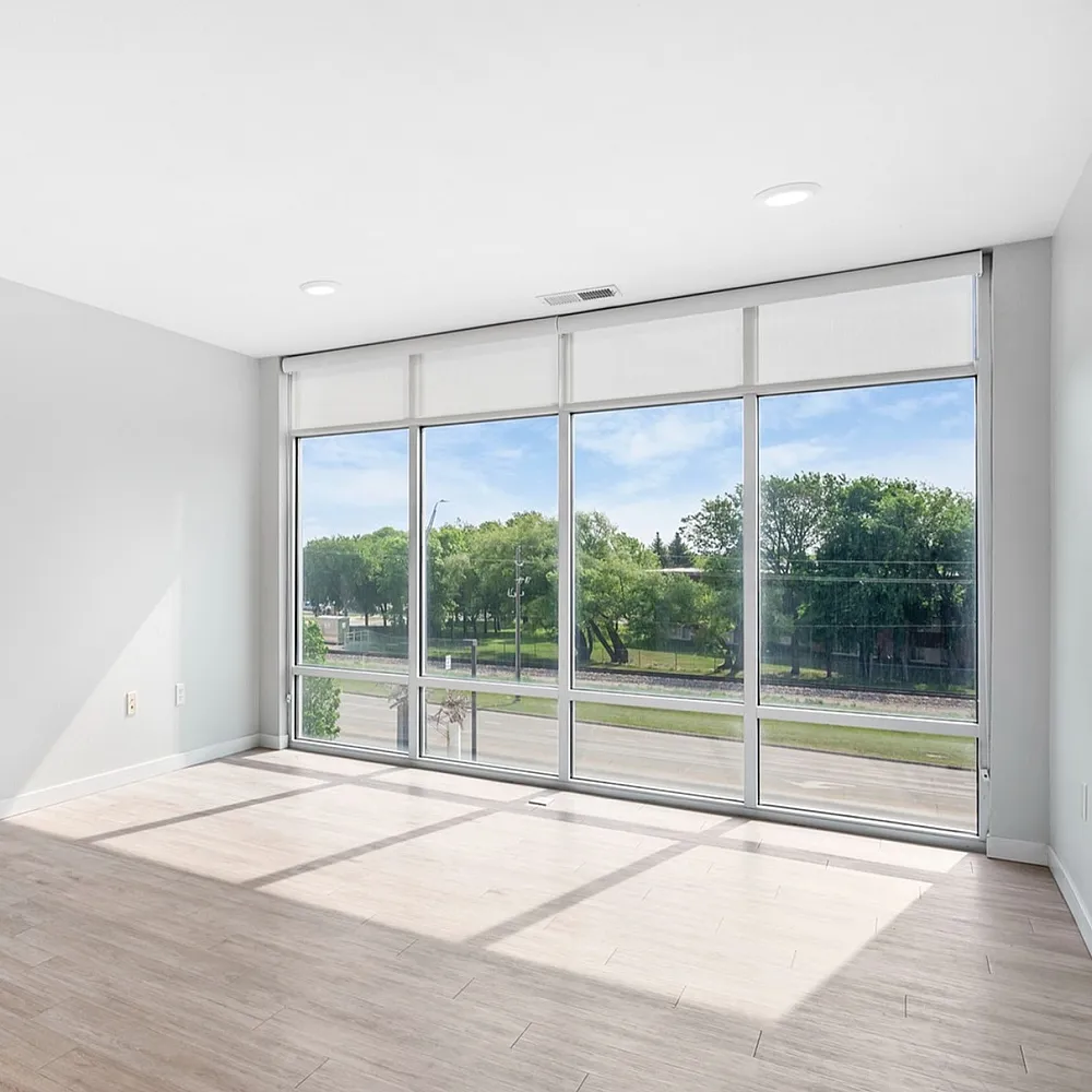 Bright, spacious apartment room with large floor-to-ceiling windows offering scenic views of green trees and clear blue skies.
