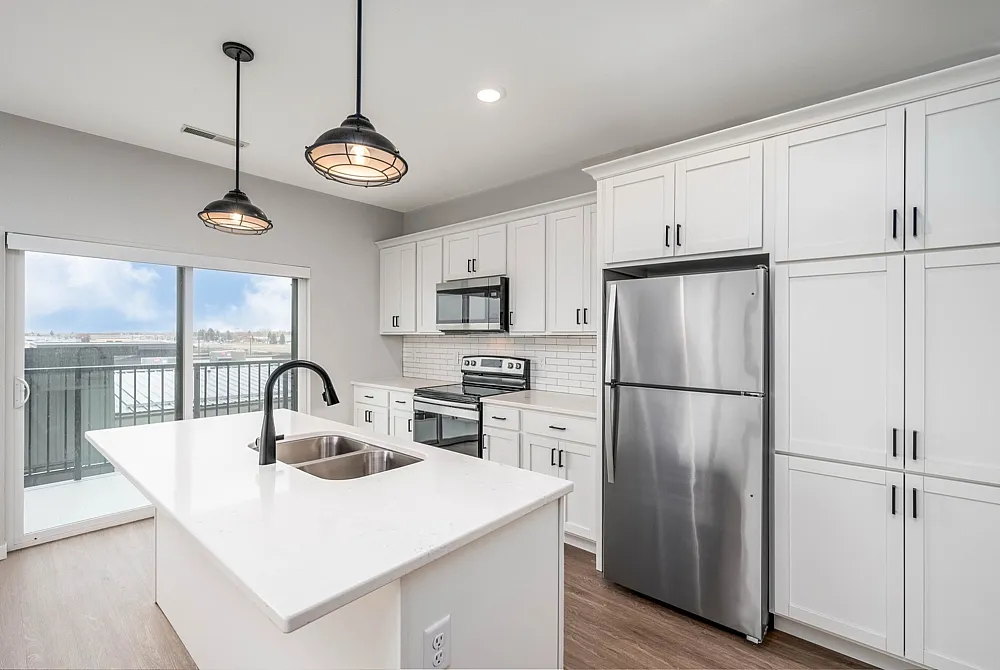 Modern kitchen with sleek white cabinetry, stainless steel appliances, and a bright open layout featuring a central island with a double sink.