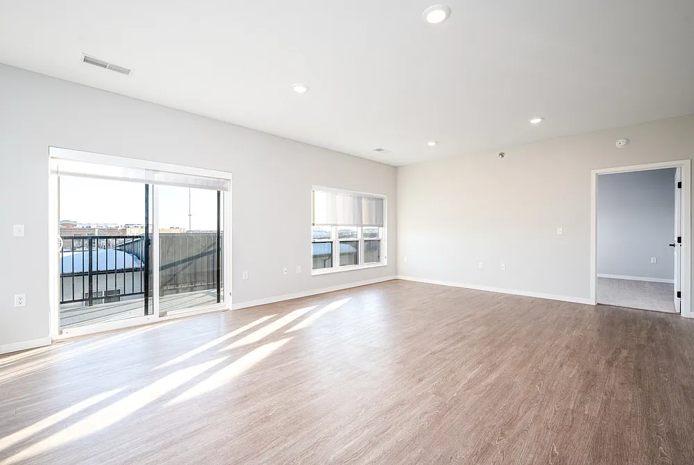 Bright and spacious living area with sleek hardwood floors, large windows for natural light, and balcony access, perfect for modern living.
