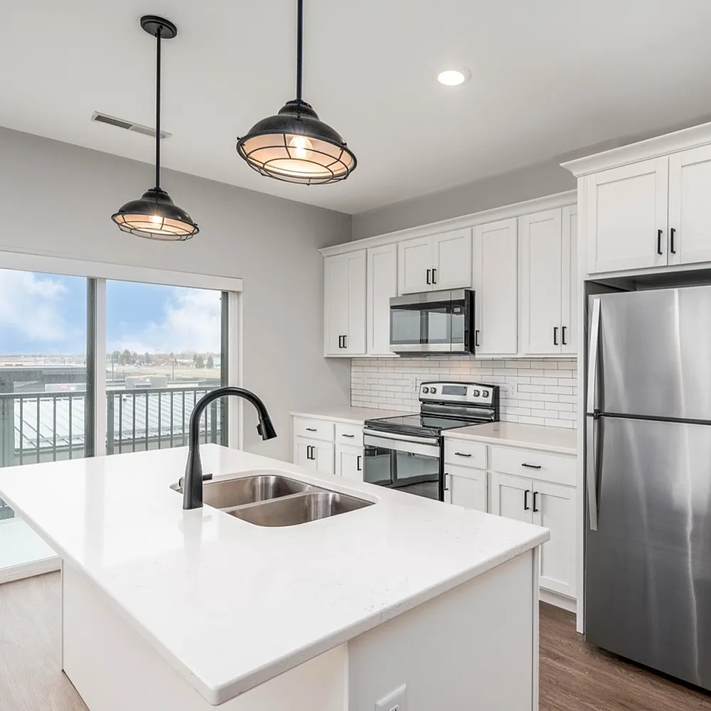 Bright modern kitchen with sleek white cabinetry, stainless steel appliances, and an inviting island, featuring large windows with a balcony view.