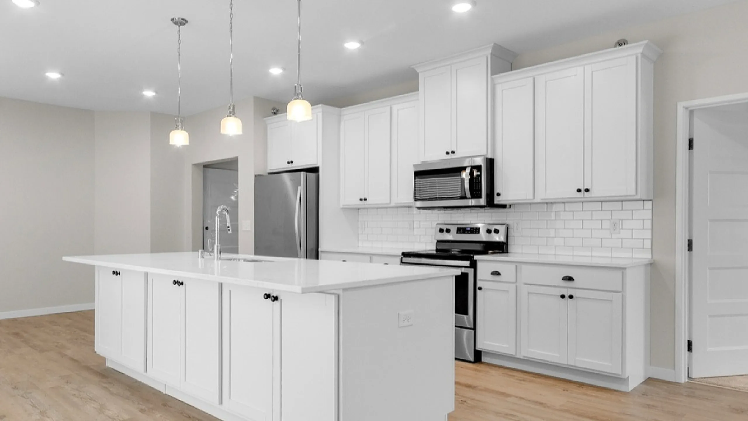 Modern kitchen with stylish white cabinetry, sleek island, and stainless steel appliances, complemented by elegant wooden floors.