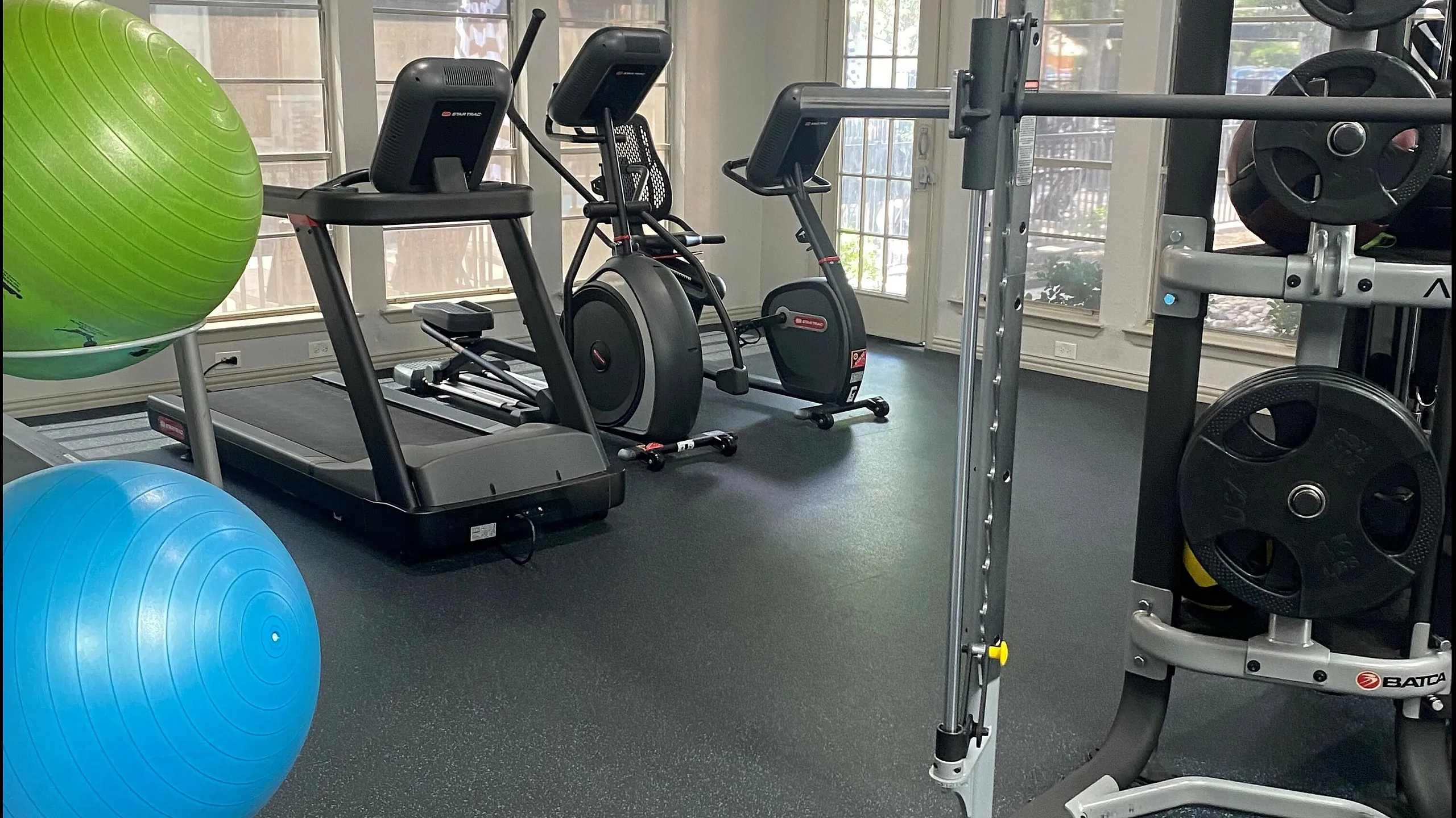 Modern fitness center equipped with treadmills, stationary bikes, weight machine, and vibrant stability balls in a well-lit space.