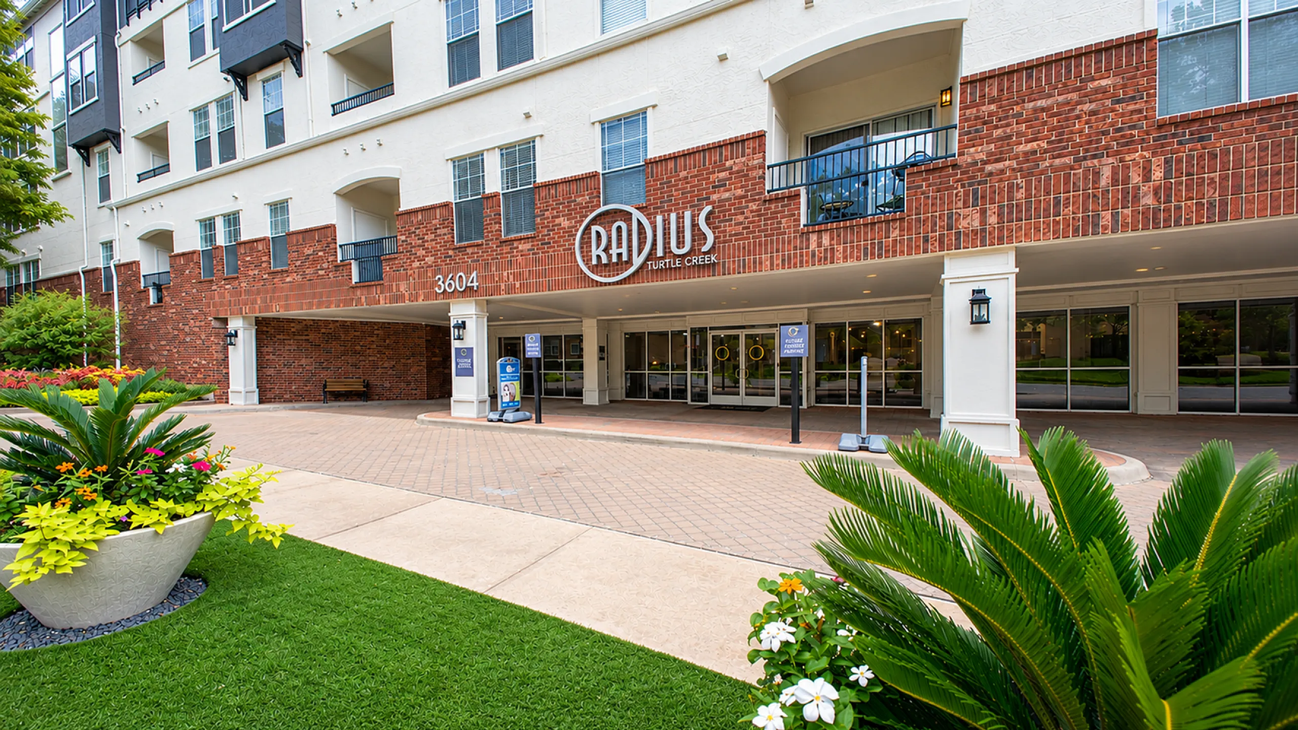 Inviting apartment entrance with lush greenery and vibrant floral displays, featuring contemporary architectural design and a welcoming atmosphere.