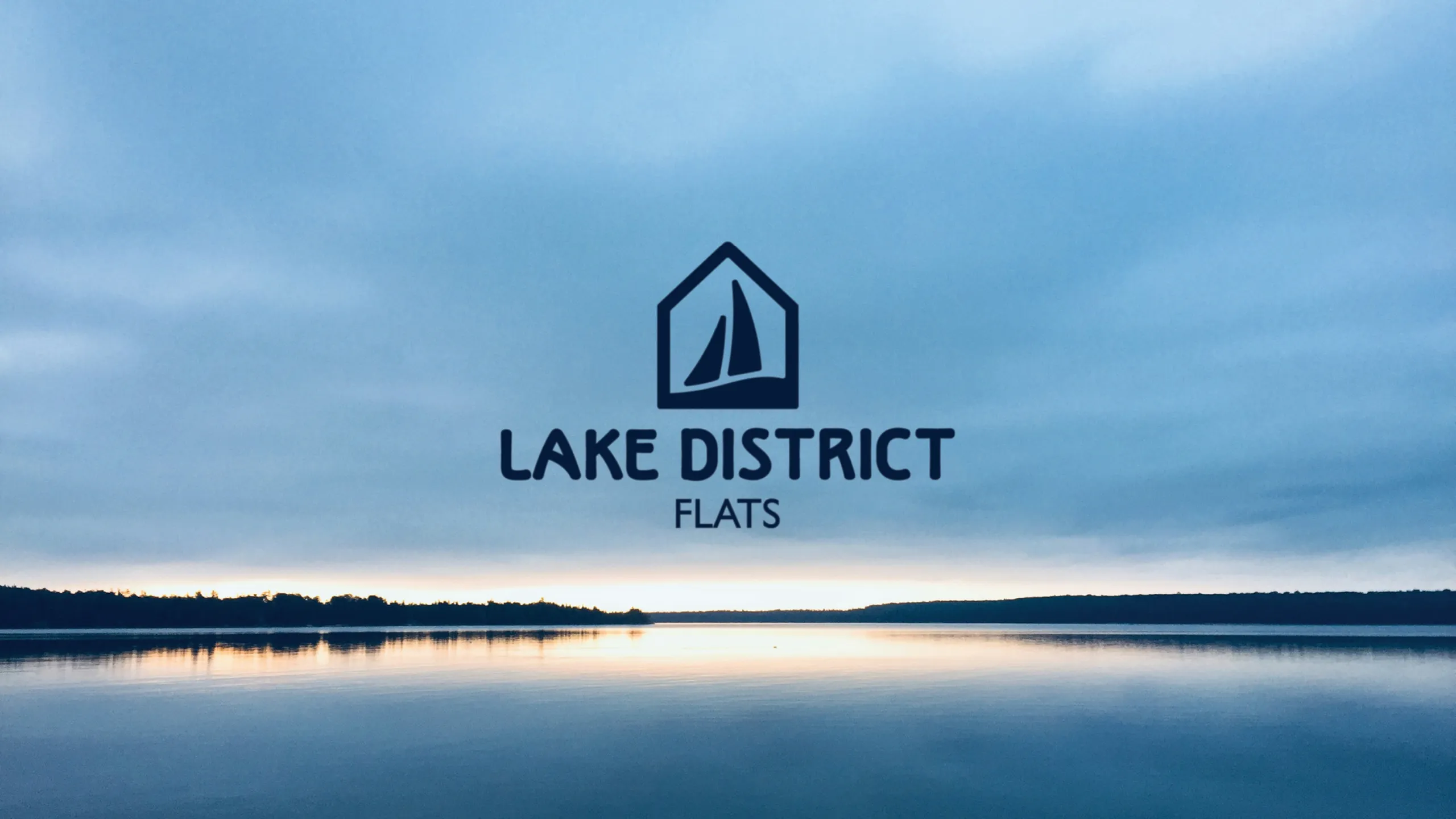Serene lake view at dusk with Lake District Flats logo, promising tranquil living in nature's embrace.