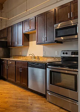 Inviting loft-style kitchen with exposed brick, sleek stainless steel appliances, and chic wooden cabinetry complemented by a modern granite island.