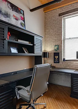 Chic home office with a modern desk, black shelving unit, and cozy gray chair set against a stylish brick wall, perfect for productivity.