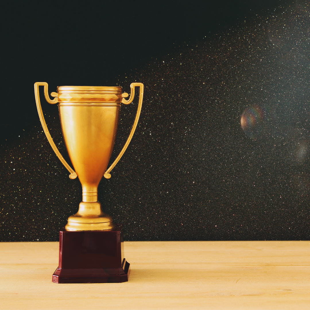 Gold cup award against a solid black background with glitter in the background.