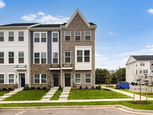 Modern townhouse exterior with stylish multi-story design, brick and siding facade, manicured lawns, and vibrant neighborhood setting under a clear blue sky.