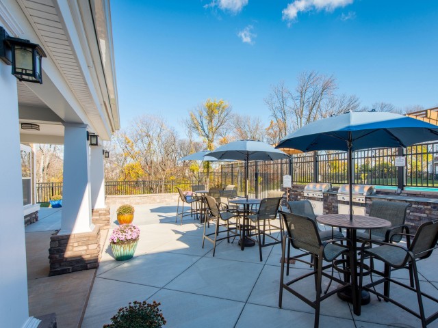 Outdoor dining area with tables and umbrellas outside the clubhouse patio at Prospect Hall Apartments.