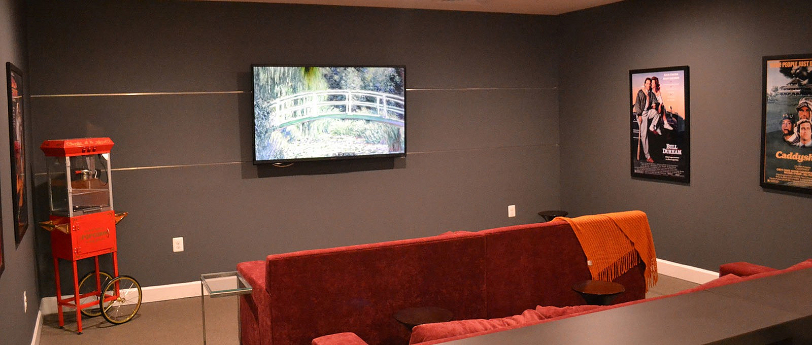 Chic entertainment room with cozy red seating, modern TV setup, classic movie posters, and a charming popcorn machine for a cinematic experience.