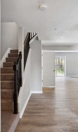 Hallway at 6302 Jacobs Court with carpeted stairs, black railings, gray paint, and spacious open-concept living area with paned window doors to private patio