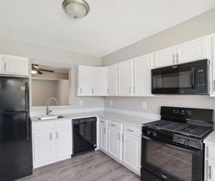 Renovated kitchen at Jacobs Court showing black appliances, upgraded white cabinets & countertops, and cut through window to the living room.