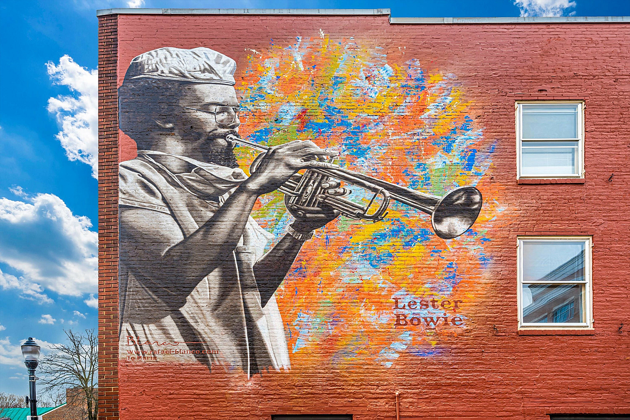 Colorful mural of a trumpet player against a bright, multicolored background on a brick building.