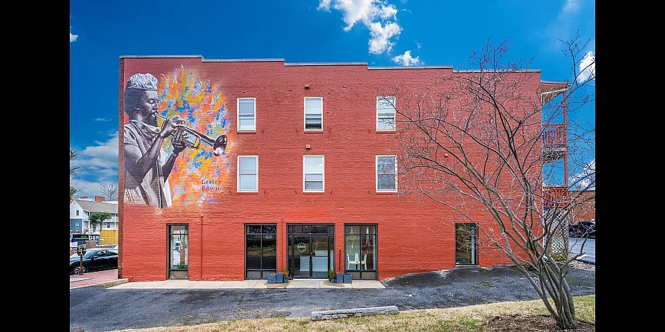 Bold red brick building with colorful mural and bright blue sky, showcasing urban charm.