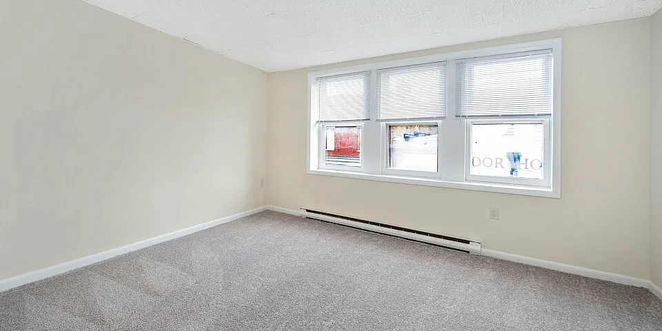 Bright and spacious room with large windows and neutral carpeting.