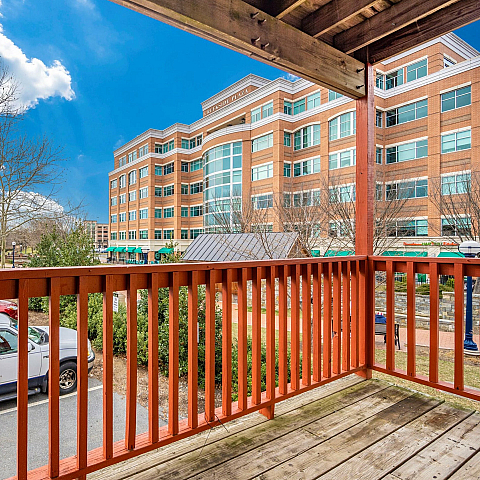 Beautiful view from a wooden balcony overlooking a bustling urban plaza with red-brick buildings and vibrant greenery.