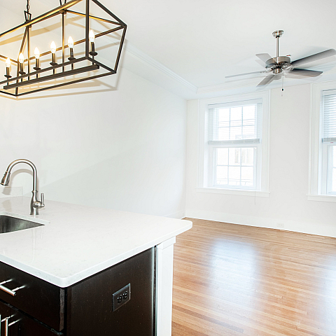 Bright kitchen area with modern chandelier, sleek countertops, and spacious wood flooring.