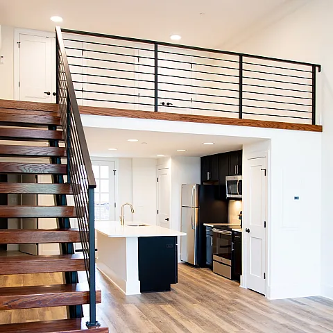Chic loft interior featuring a wooden staircase, open-concept kitchen, and mezzanine level.