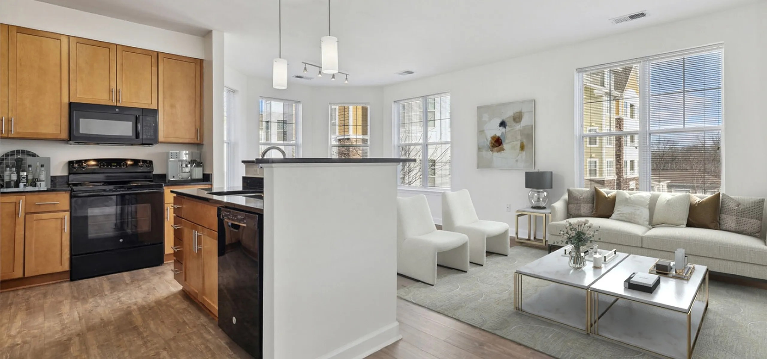 Bright and modern open-concept kitchen and living area with stylish wood cabinetry, elegant lighting, and large windows offering natural light.