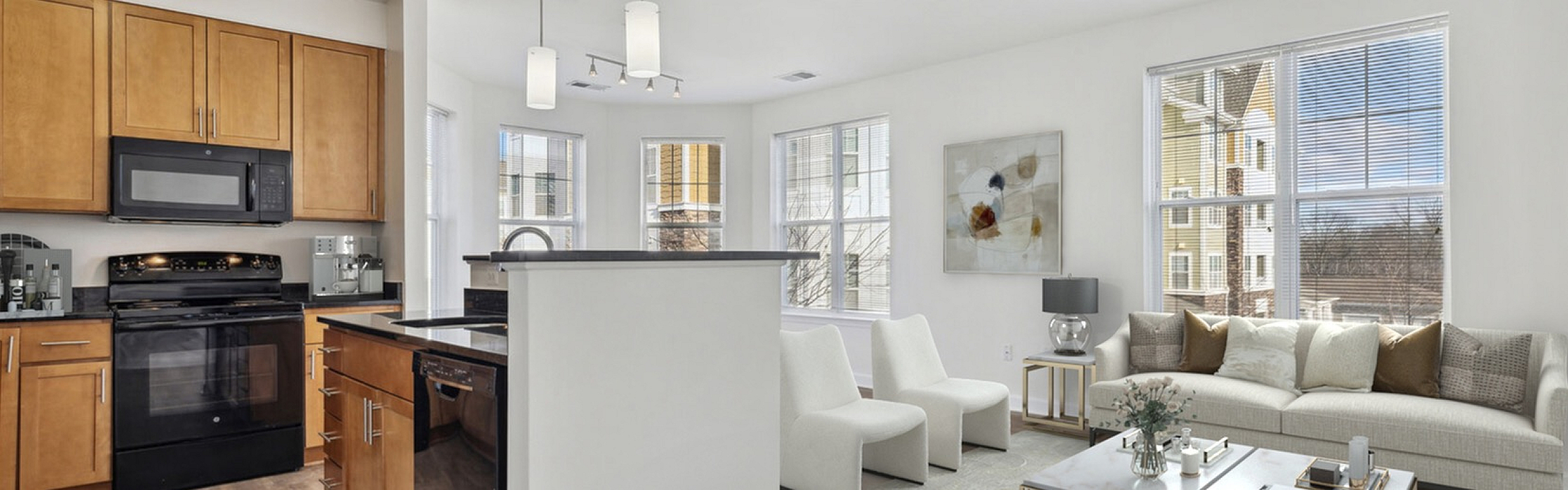 Bright and modern open-concept living room and kitchen with sleek wood flooring, stylish light fixtures, and abundant natural light from large windows.