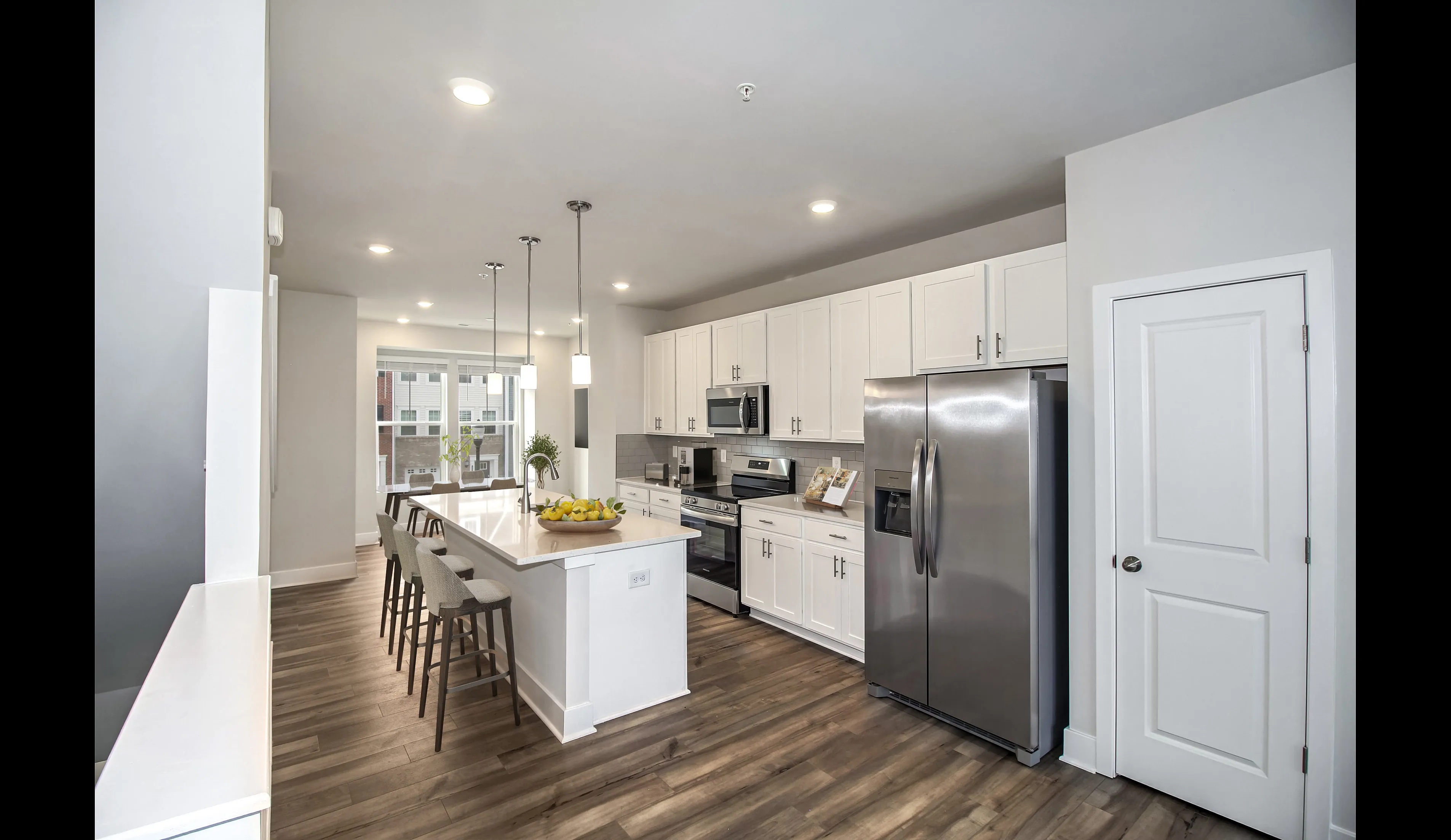 Modern kitchen at The Terrace at Sycamore Ridge showing white Shaker Cabinets, vinyl plank flooring, stainless steel appliances, pendant lighting, and a white stone countertop with a kitchen island.